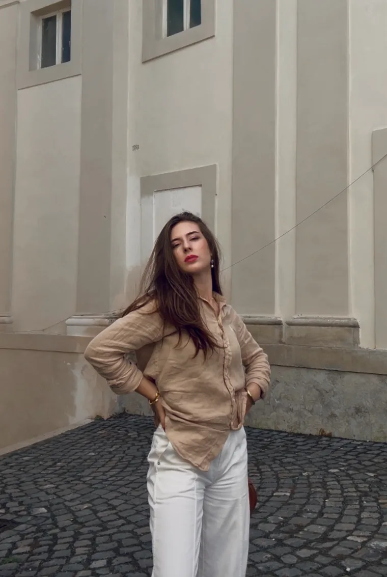 Portrait in a linen shirt against a pale wall on a cobblestone street.